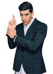 Handsome hispanic man wearing business clothes holding symbolic gun with hand gesture, playing killing shooting weapons, angry face