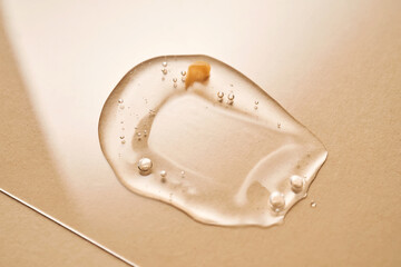 A drop of transparent cosmetic gel on a beige background.