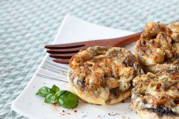 Stuffed mushrooms with melted cheese, vegetables, and spices on a plate with a wooden fork. Close-up. Selective focus. Healthy vegetarian appetizer or party food.