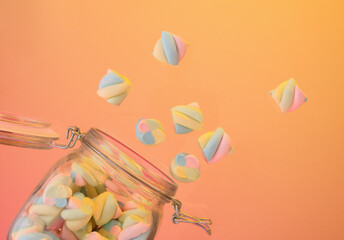 Marshmallows fly out of the glass jar. Colorful and bright sweets.
