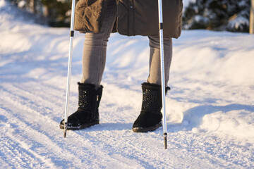 female legs in ugg boots on a snowy road. she travels through snowy landscapes with Nordic walking...