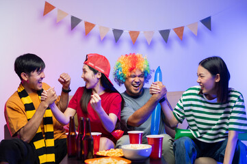 Group of Asian male and female friends Watch the World Cup live broadcast on TV. Sports fans shout...