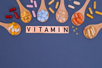 Different vitamins in wooden spoons with text on gray background