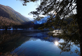 sun  behind the mountains and the reflection of the mountains on the alpine lake in cold winter...