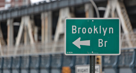 brooklyn bridge sign on the side of the road in downtown brooklyn, new york city (famous landmark travel destination signage in nyc) isolated close up out of focus manhattan bridge background
