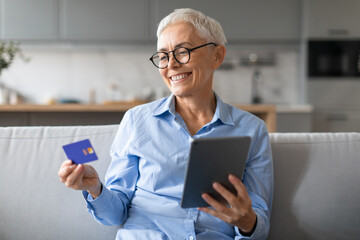 mature woman holding credit card websurfing on digital tablet indoor