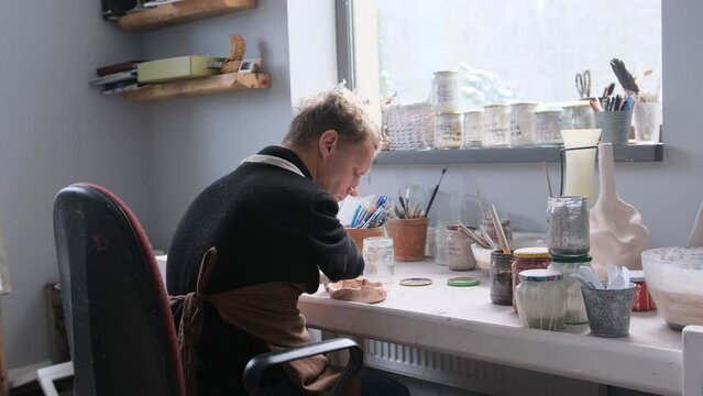 a young man with congenital hand pathology paints pottery with enamel in the workshop.