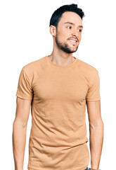 Fototapeta premium Hispanic man with beard wearing casual t shirt looking away to side with smile on face, natural expression. laughing confident.