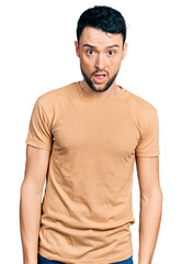 Fototapeta premium Hispanic man with beard wearing casual t shirt in shock face, looking skeptical and sarcastic, surprised with open mouth
