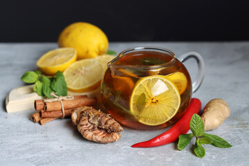 Glass teapot with ginger tea, lemon, turmeric root and mint on grey background with space for text. Cold and flu season concept. 