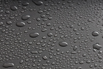 top view of a black surface with water droplets of various shapes