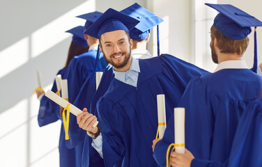 Students graduation ceremony, happy adult students in row wearing complete outfit cap and blue...