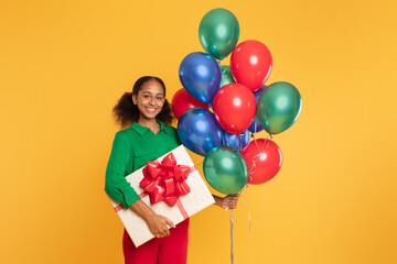 Fototapeta na wymiar african teenager girl holds bunch of balloons and gift, studio