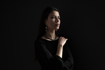 A woman wearing a black dress stands alone in a dark setting.