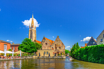 Fototapeta premium Bakkersrei water canal with tourist boat, Catholic Church of Our Lady Gothic style and Sint-Janshospitaal building in Brugge old town quarter, Bruges city historical centre, Flemish Region, Belgium