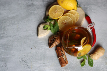 Glass teapot with ginger tea, lemon, turmeric root and mint on grey background with space for text. Cold and flu season concept. 