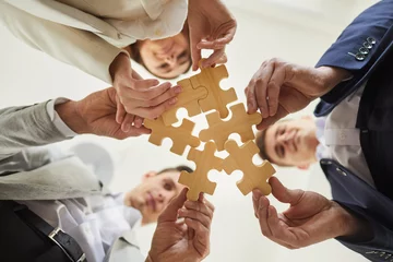 Foto op Canvas Business team trying to find solution to problem together. Group of young people holding parts of jigsaw puzzle. Crop shot close up bottom view from below hands holding wooden pieces. Teamwork concept © Studio Romantic