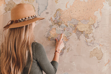 Rear view of blonde woman with hat pointing vintage map with his finger