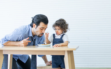 Fototapeta na wymiar Caucasian handsome father eating spaghetti or pasta together with his little cute daughter at home after work. Family and Education Concept.