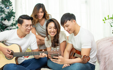 Group of asian friends having party, playing guitar and singing together with fun in living room at home. Lifestyle Concept.