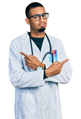 Young african american man wearing doctor uniform and stethoscope pointing to both sides with fingers, different direction disagree