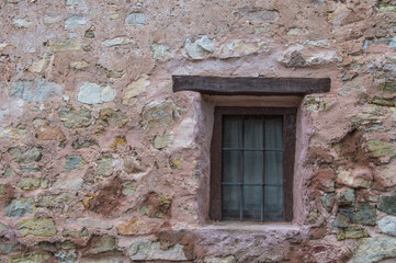 rustic window with wooden beam and grille on a reddish stone wall