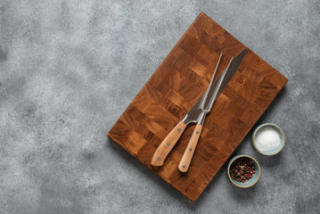Culinary background with wooden cutting board, knife, meat fork and spices. Top view, flat lay, copy space.