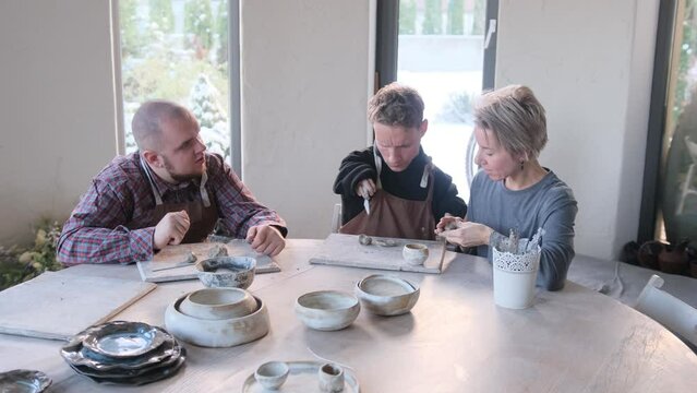 A volunteer girl helps two guys with physical and mental disabilities to do clay modeling. Development of fine motor skills.