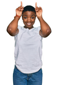 Young african american woman wearing casual white t shirt doing funny gesture with finger over head as bull horns