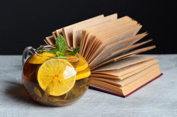 Glass teapot with ginger and lemon tea, open book and reading glasses on a table. Winter day still...