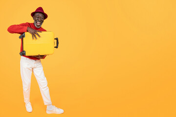 Joyful African American senior in a red sweater and trendy red hat carrying a bright yellow suitcase