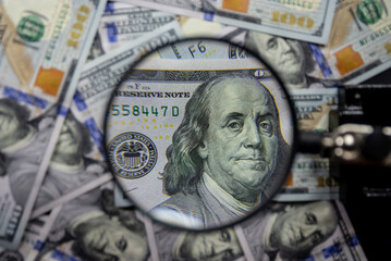 100 american dollar notes background with Benjamin Franklin face portrait magnified with a magnifying glass. Monetary wallpaper.