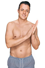 Fototapeta premium Handsome young man wearing swimwear shirtless clapping and applauding happy and joyful, smiling proud hands together