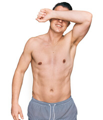 Handsome young man wearing swimwear shirtless covering eyes with arm smiling cheerful and funny. blind concept.