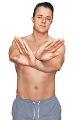 Fototapeta premium Handsome young man wearing swimwear shirtless rejection expression crossing arms doing negative sign, angry face