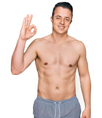 Handsome young man wearing swimwear shirtless smiling positive doing ok sign with hand and fingers. successful expression.