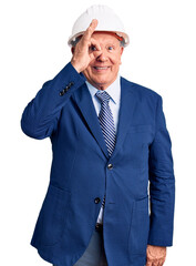 Senior handsome grey-haired man wearing suit and architect hardhat doing ok gesture with hand smiling, eye looking through fingers with happy face.