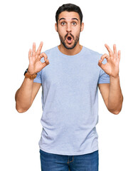 Naklejka premium Young hispanic man wearing casual clothes looking surprised and shocked doing ok approval symbol with fingers. crazy expression