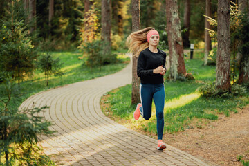 Female runner in vibrant sportswear jogging in a lush park at sunrise.