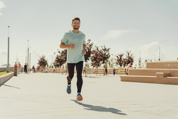 Man in a casual t-shirt jogging happily on a sunny waterfront promenade.