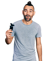 Hispanic man with ponytail holding electric razor machine scared and amazed with open mouth for...