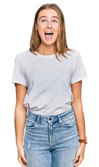 Obraz premium Beautiful young blonde woman wearing casual white t shirt angry and mad screaming frustrated and furious, shouting with anger. rage and aggressive concept.