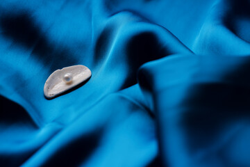 natural freshwater pearls in a river shell lie on a background of blue silk fabric. empty space for text