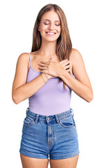 Fototapeta premium Young beautiful blonde woman wearing casual style with sleeveless shirt smiling with hands on chest with closed eyes and grateful gesture on face. health concept.