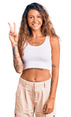 Young hispanic woman with tattoo wearing casual clothes smiling with happy face winking at the...