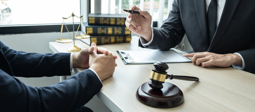 Male lawyer working on documents contract papers of the important case with the business customer and wooden gavel, brass scale in office