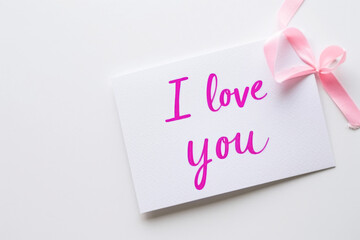 I love you message with pink ribbon and white card on white background