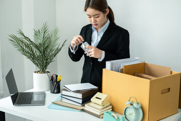 Business woman employee in suit packing id card of office worker and personal belongings into brown cardboard box