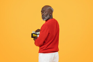 Skeptical elderly African American man in a red sweater discreetly holding a wallet