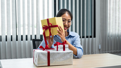 Young asian woman with many presents and holding gold gift box on her desk